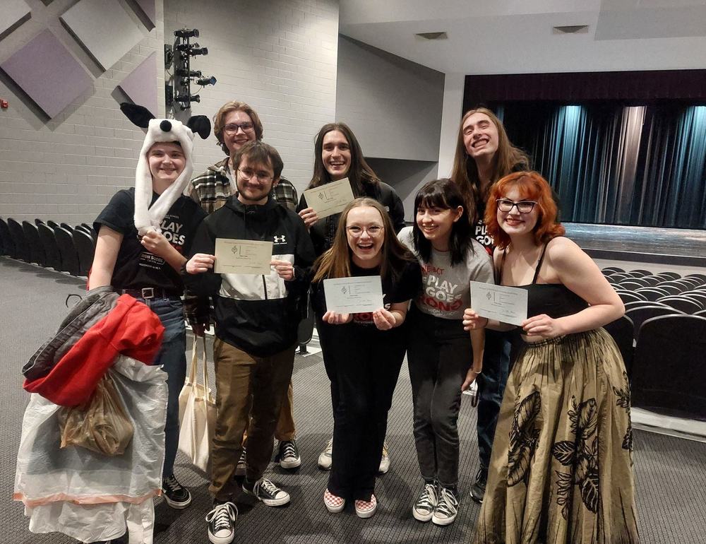 theatre students grinning and holding certificates in an auditorium